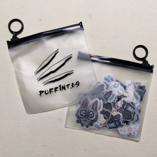 A clear plastic zippered bag with the text 'PURRINT.ES' and logo on it, displayed next to a collection of various stickers and small items inside.